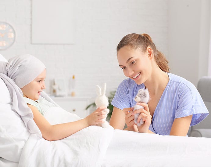 nurse smiling at hospital bedside of child who is playing with a toy rabbit having undergone treatments for brain tumours