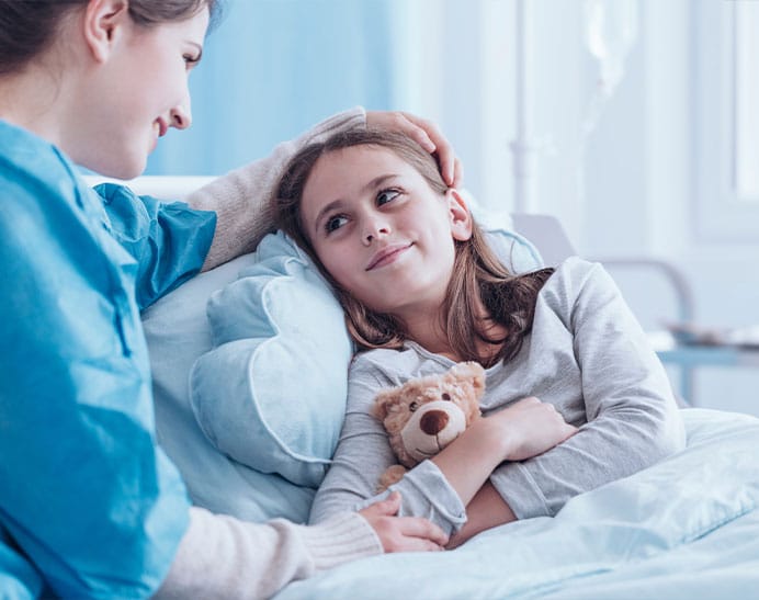 nurse with child before going in for tests for brain tumours. Nurse is comforting her with a hand on her head and her arm, whilst the child cuddles their teddy bear