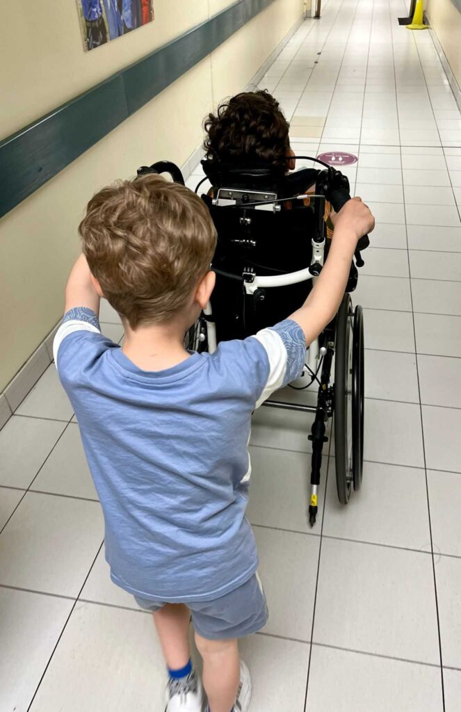 Tomos pushing Olivers wheelchair down a hospital corridor